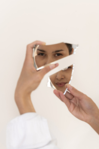 A woman looking at her reflection in a broken mirror, symbolizing the fragmented self-esteem often shaped by narcissistic parents.