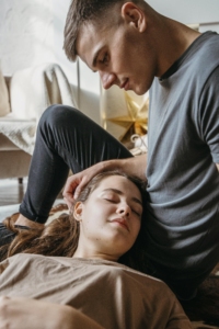 A woman resting peacefully with her head on a man’s lap while he gently touches her hair, showing comfort, safety, and emotional closeness.